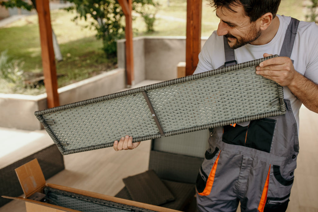 Worker assembling furniture on a terrace, smiling while unpacking cardboard boxes and enjoying the outdoor space of a new home